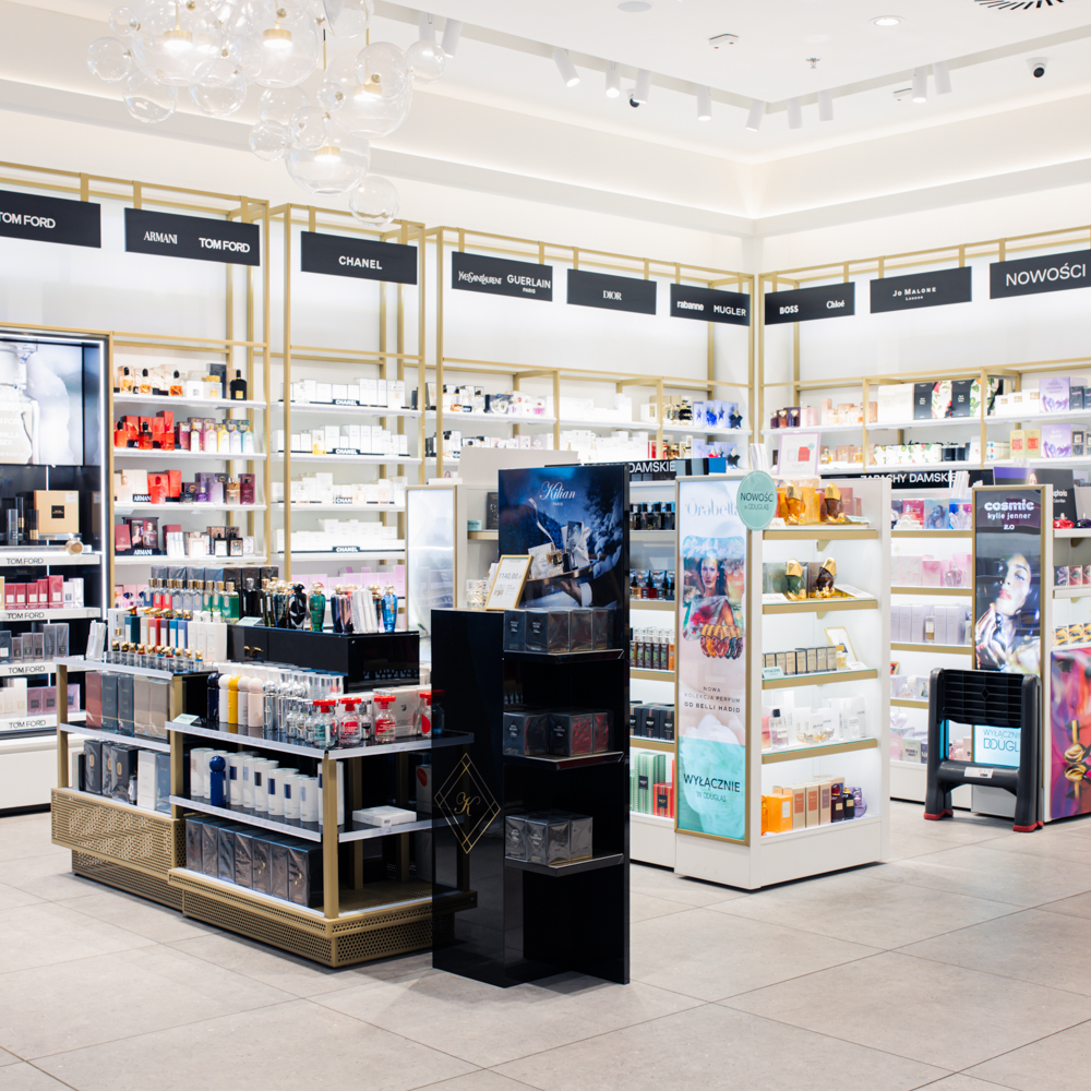 Przejrzysta ekspozycja kosmetyków do makijażu i pielęgnacji w salonie Douglas; rzędy podświetlanych regałów z produktami premium.