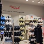 Przejrzysta aranżacja wnętrza salonu Triumph w Szczecinie z licznymi standami oferującymi różne modele biustonoszy i majtek.