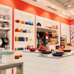 Ekspozycja kultowych żeliwnych garnków i patelni Le Creuset w intensywnych kolorach na regałach salonu w Galaxy.