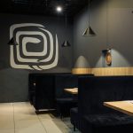 Elegancka strefa wypoczynkowa w restauracji Unagi Sushi w Centrum Galaxy z wygodnymi czarnymi kanapami i logo restauracji na ścianie.