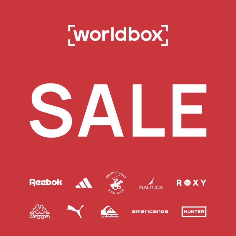 Grafika reklamowa marki Worldbox przedstawia duże, białe hasło „SALE” umieszczone w centralnej części na jednolitym, czerwonym tle. W górnej części widnieje logo sklepu, natomiast na dole rozmieszczono mniejsze logotypy popularnych marek streetwearowych i sportowych, takich jak Reebok, Adidas czy Puma.