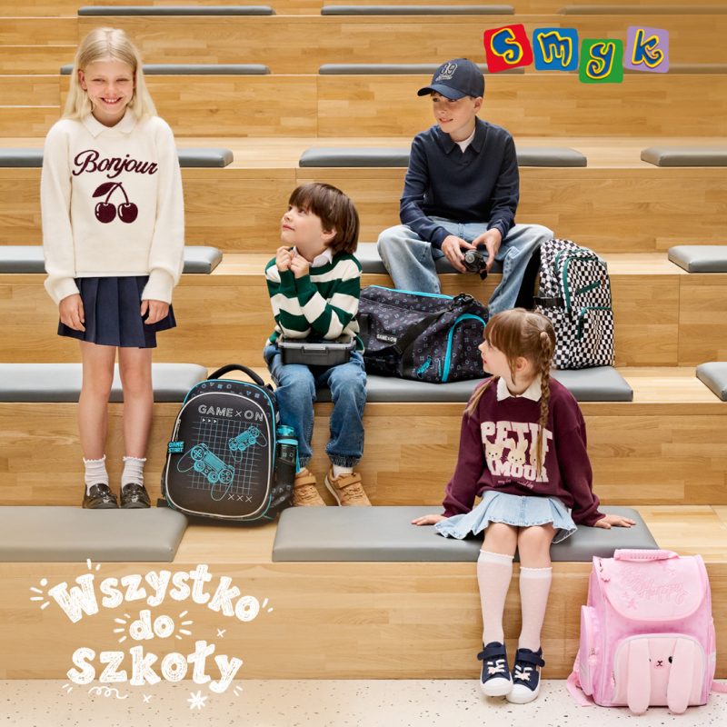 Grafika przedstawia dzieci w szkolnych stylizacjach pozujące na drewnianych stopniach w otoczeniu plecaków i akcesoriów. W lewym dolnym rogu znajduje się biały napis „Wszystko do szkoły”, a w prawym górnym rogu umieszczono kolorowe logo marki Smyk.