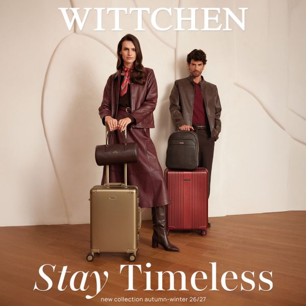 Zdjęcie wizerunkowe kampanii Wittchen „Stay Timeless” na sezon jesień-zima 26/27. Po lewej stronie stoi kobieta w skórzanej, bordowej kurtce i spódnicy oraz wysokich kozakach, trzymająca złotą walizkę podróżną z zamontowanym na niej małym kuferkiem. Po prawej stronie stoi mężczyzna w brązowej skórzanej kurtce, trzymający bordową walizkę z postawionym na niej plecakiem. U góry widnieje białe logo WITTCHEN, a u dołu napis „Stay Timeless new collection autumn-winter 26/27”.
