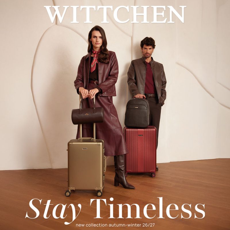Zdjęcie wizerunkowe kampanii Wittchen „Stay Timeless” na sezon jesień-zima 26/27. Po lewej stronie stoi kobieta w skórzanej, bordowej kurtce i spódnicy oraz wysokich kozakach, trzymająca złotą walizkę podróżną z zamontowanym na niej małym kuferkiem. Po prawej stronie stoi mężczyzna w brązowej skórzanej kurtce, trzymający bordową walizkę z postawionym na niej plecakiem. U góry widnieje białe logo WITTCHEN, a u dołu napis „Stay Timeless new collection autumn-winter 26/27”.