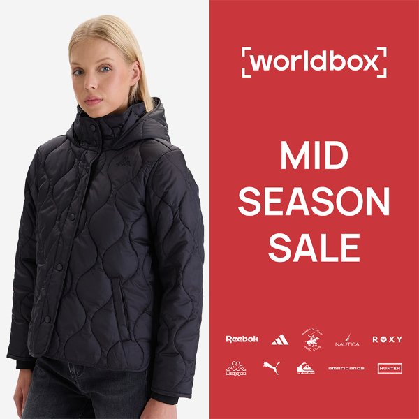 Grafika promocyjna sieci Worldbox informująca o wyprzedaży „MID SEASON SALE”. Na czerwonym tle w prawej części widoczne są białe napisy oraz logotypy marek partnerskich, takich jak Reebok, Adidas, Beverly Hills Polo Club, Nautica, Roxy, Kappa, Puma, Quiksilver, Americanos i Hunter. W lewej części na jasnym tle pozuje blond modelka ubrana w czarną, pikowaną kurtkę z wysokim kołnierzem i kapturem oraz ciemne spodnie.