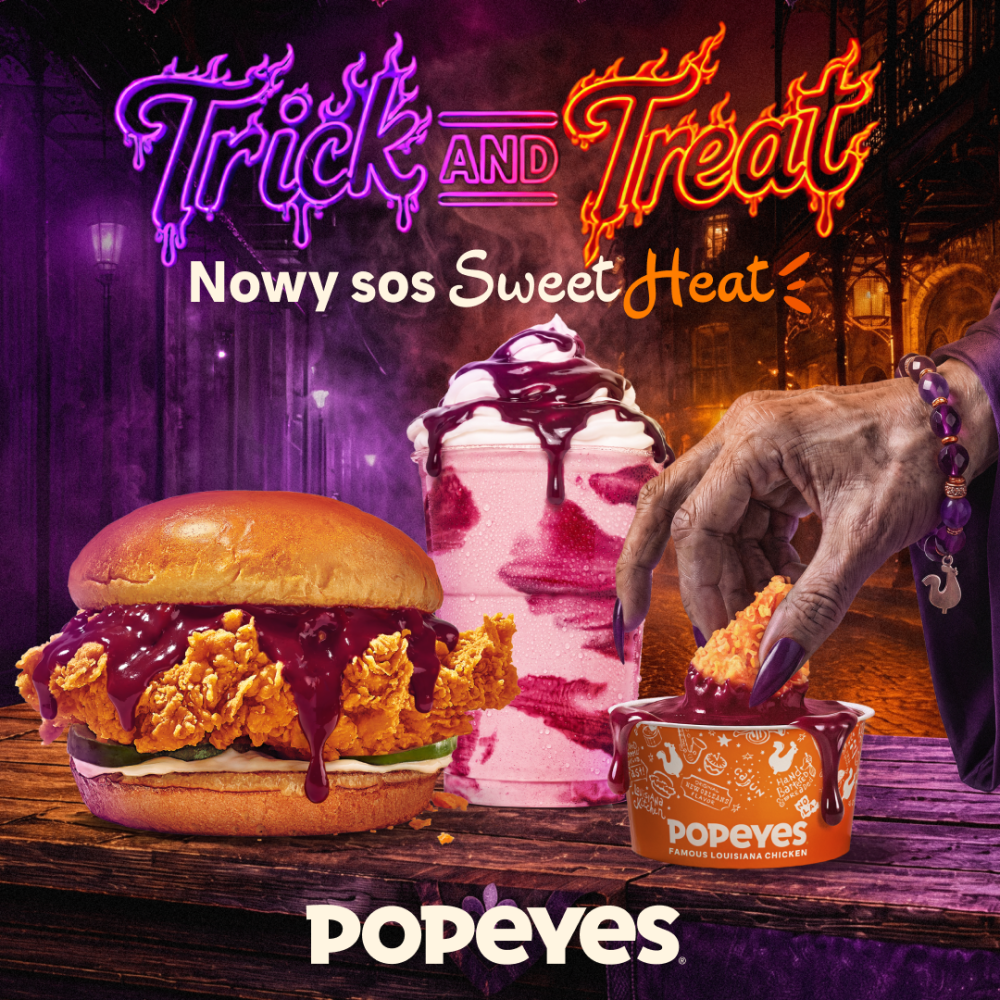 Grafika promocyjna sieci Popeyes z okazji Hallowen prezentująca nowy sos Sweet Heat. Na mrocznym, fioletowym tle z motywem ulicy i latarni umieszczono neonowy napis „Trick AND Treat” oraz tekst „Nowy sos Sweet Heat”. W centralnej części widoczny jest duży burger z panierowanym kurczakiem oblanym ciemnym sosem, koktajl z polewą oraz ręka wampira z fioletową bransoletką, która moczy strips w małym kubeczku z logo marki Popeyes. W dolnej części grafiki znajduje się białe logo „POPEYES”.