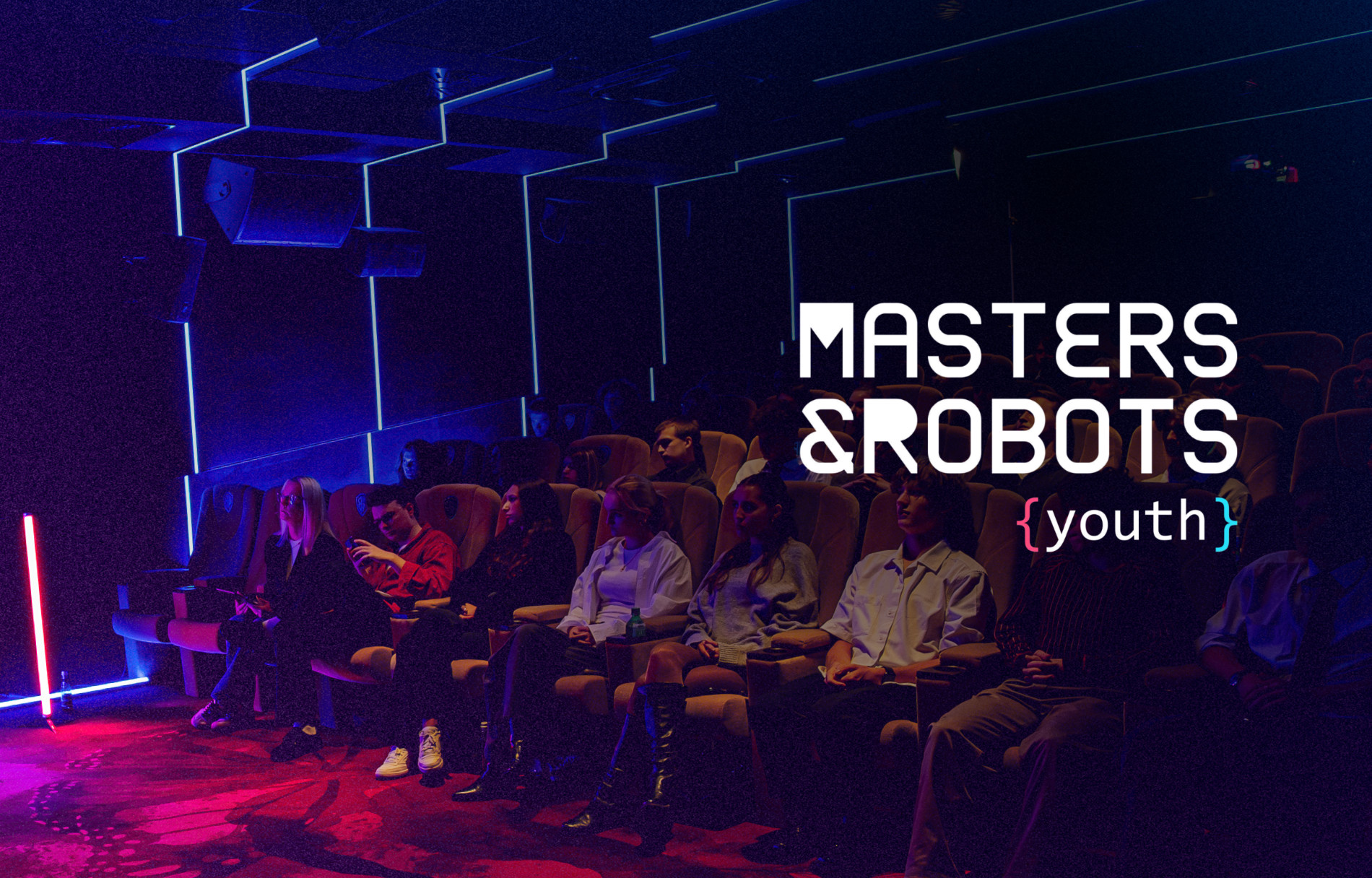 Grafika promocyjna konferencji „Masters & Robots {youth}”. Na zdjęciu widoczna jest zaciemniona sala kinowa z rzędami foteli, w których siedzą uczestnicy wydarzenia. Wnętrze oświetlone jest nastrojowym, niebieskim i czerwonym światłem. W prawej części grafiki znajduje się biały napis z tytułem konferencji „MASTERS & ROBOTS {youth}”.